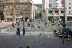 Blick auf den Johannes Rau-Platz mit im Sand spielenden Kindern von der Rathaustreppe aus
