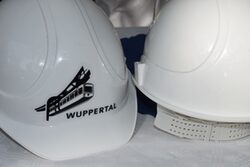Zwei weiße Bauhelme, auf einem ist eine Schwebebahngrafik und das Wort "Wuppertal" zu sehen.