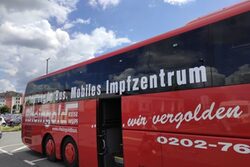 Ein roter Bus mit der Aufschrift "Mobiles Impfzentrum" vor blauem Himmel mit weißen Wolken