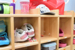 Ein Regal in einem Kindergarten mit Schuhen, Mütze, Zahnputzbecher und Brotdosen