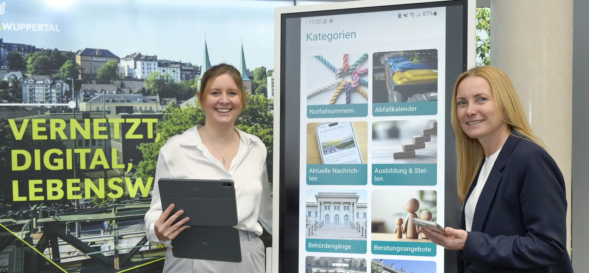 OB Miriam Scherff und Dezernentin Sandra Zeh stehen vor einem Bildschirm, auf dem die Stadt-App angezeigt wird