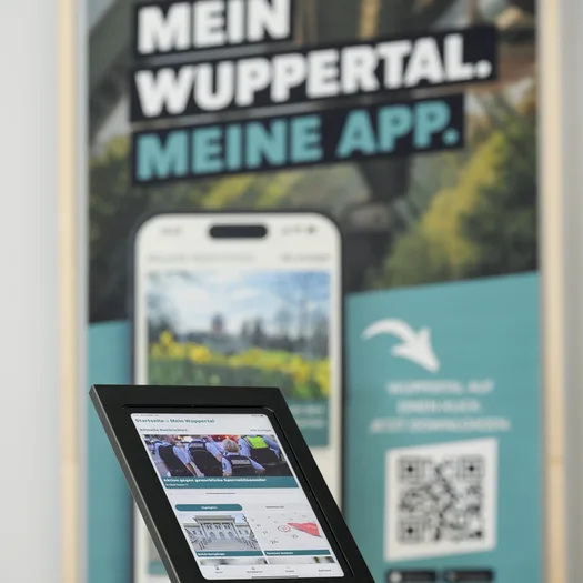 Ein Bildschirm zeit die Wuppertal-App. Im Hintergrund ein Banner mit der Aufschrift "Mein Wuppertal. Meine App."