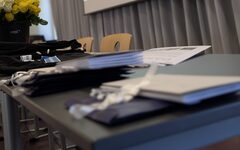 Schulraum mit Leinwand, auf der eine Präsentationsfolie zum Thema Toleranz und Vielfalt gezeigt wird. Im Vordergrund liegen auf einem Tisch Tagungsmaterialien und Blumen