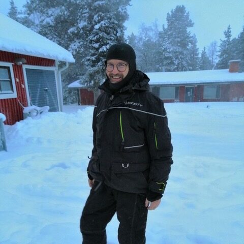Ein Mann mit dicker Winterkleidung in einem verschneiten Dorf in Finnland.