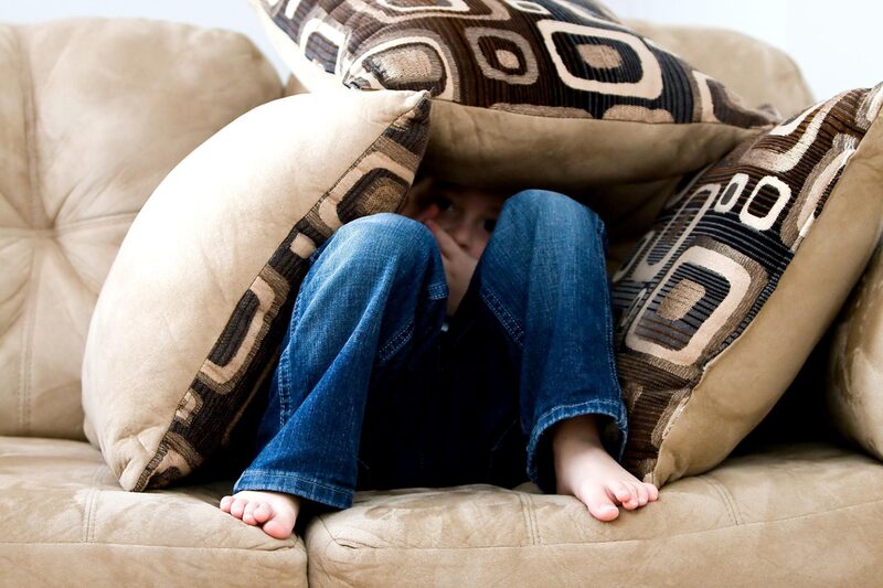 Junge auf einem Sofa begraben unter Kissen