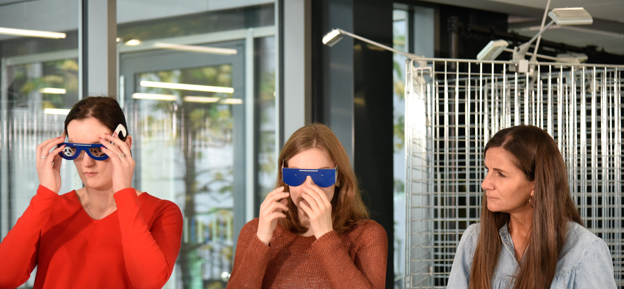 Zu sehen sind drei Frauen, die Brillen testen, welche Sehbehinderungen simulieren.
