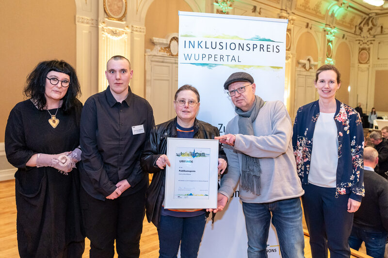 Fünf Personen stehen vor dem Banner Inklusionspreis Wuppertal und halten die Urkunde für den Publikumspreis in den Händen.