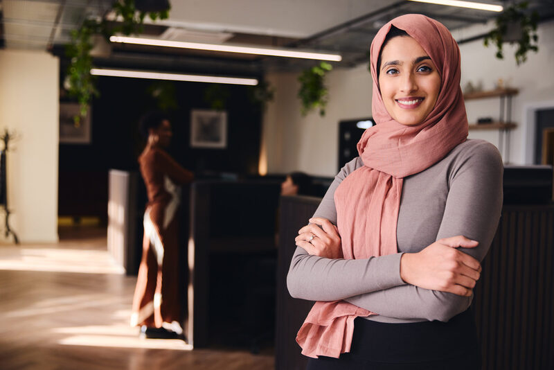 Portrait of confident young Middle Eastern woman smiling and looking at camera in coworking space