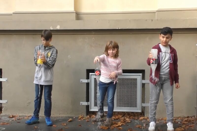 drei Kinder schütten Wasser aus Plastikflaschen