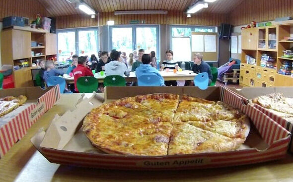 Pizzaschachtel im Vordergrund und im Hintergrund die Kindergruppe