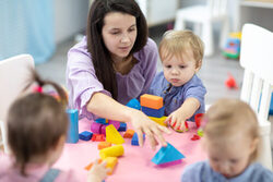 Female teacher sitting at table in playroom with three kindergarten children constructing