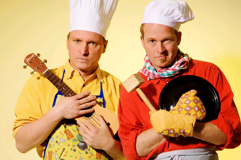 Zaches und Zinnober: Zwei Köche mit Kochmützen halten Topfdeckel und eine Ukulele im Arm