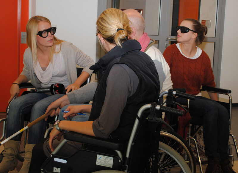 Journalisten setzen sich in den Rollstuhl und "proben" mit Herrn Engels das Rollstuhlfahren im Rathaus.