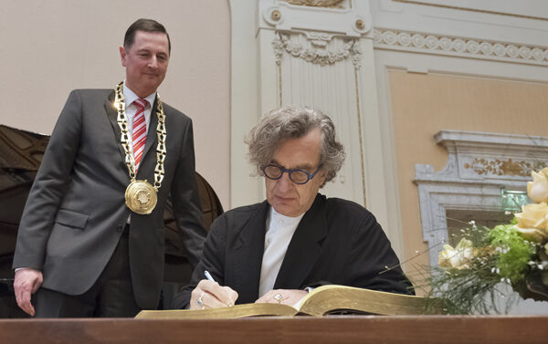 Wim Wenders trägt sich ins Goldene Buch der Stadt ein, OB Peter Jung trägt die Amtskette und steht hinter ihm.