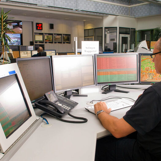Ein Mitarbeiter der Feuerwehrleitstelle an seinem Arbeitsplatz, vor ihm sein Telefon und mehrere Bildschirme.