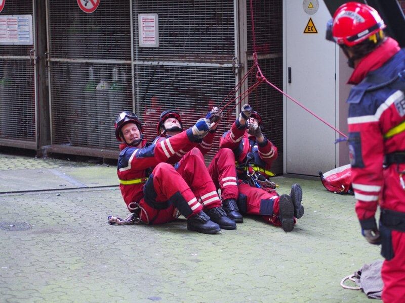 Drei Feuerwehrleute halten mit ganzer Kraft am Boden ein Seil.