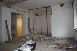 Der Blick in den Raum: eine Wand ist abgerissen und der Schutt liegt auf dem Boden, einige Leitungen ragen aus der Wand.