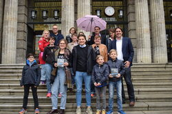 Die Gewinner freuen sich über ihre Preise auf der Rathaustreppe, darunter auch ein Regenschirm