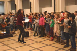 Die Singleiterin singt mit den Kindern aus dem SingPausen-Projekt im Lichthof des Rathauses.