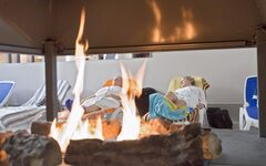 Saunafeuer mit ruhenden Saunabesuchern auf Liegen im Hintergrund