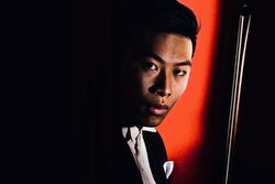 Portrait des Violinisten Kerson Leong mit Geigenbogen vor rotem Hintergrund
