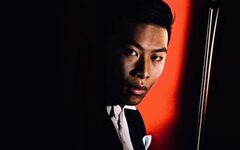 Portrait des Violinisten Kerson Leong mit Geigenbogen vor rotem Hintergrund
