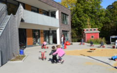 Im Außenbereich der neuen Kita Rudolfstraße laufen Kinder auf ein Dreirad zu