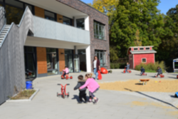 Im Außenbereich der neuen Kita Rudolfstraße laufen Kinder auf ein Dreirad zu