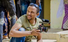 Filmemacher Eddy Munyaneza, hockend mit einer Kamera