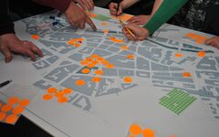 Ein Stadtplan mit vielen bunten Punkten und den Händen von Menschen, die darauf zeigen