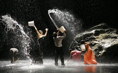 Tänzer sprühen Wasserfontänen aus Eimern auf die Bühne