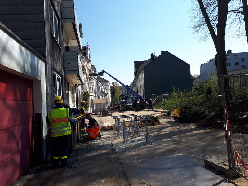 Im Vordergrund: THW-Helfer beim Sägen der Bohlen zur Sicherung des Gebäudes. Straße und Haus im Hintergrund.