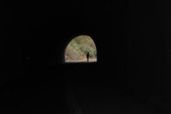 Ein Tunnel, an dessen Ende man eine grüne Böschung und eine Silhoutte eines Menschen sieht