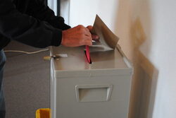 Wähler schmeißt seinen Stimmzettel in die Wahlurne