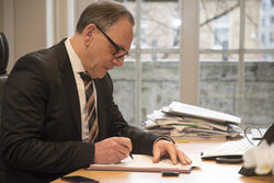 Oberbürgermeister Andreas Mucke sitzt in seinem Büro am Schreibtisch und unterschreibt ein Dokument.