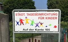 Schild mit Schriftzug: "Städt. Tageseinrichtung für Kinder" und bunten Kinderfiguren