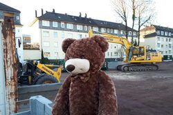 Ein Teddybär sitzt im Vordergrund einer aktuellen Kita-Baustelle mit Baggern