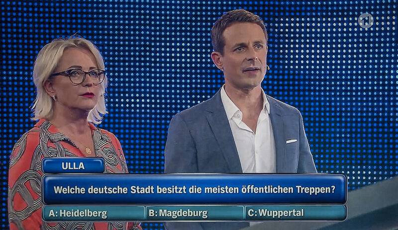 TV-Screenshot Ulla Kock am Brink und Mitspieler mit eingeblendeter Treppen-Frage