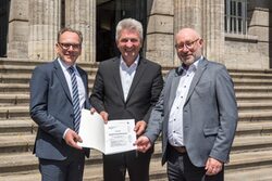 NRW-Wirtschaftsminister Dr. Andreas Pinkwart (Mitte) übergibt einen Förderbescheid an OB Andreas Mucke (Links) und Stadtdirektor Dr. Johannes Slawig. Im Hintergrund der Treppenaufgang des Rathauses.