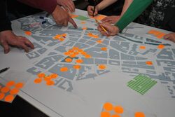 Ein Stadtplan von Elberfeld, auf den orange Punkte geklebt sind und Hände, die auf einzelne Areale zeigen