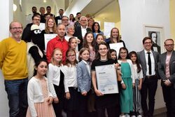 Preisträger des bundesweiten Wettbewerbs „Aktiv für Demokratie und Toleranz“ aus Nordrhein-Westfalen und Niedersachsen haben sich im Rathaus Barmen auf einer Treppe versammelt und halten ihre Urkunden in die Kamera.