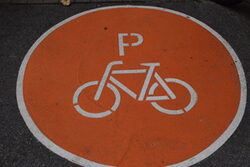 Auf dem Boden befindet sich ein orangefarbener Kreis, darin ist ein weißes Fahrrad in Piktogramm-Optik zu sehen.