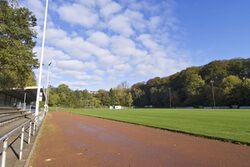 Symbolbild: Blick auf Laufbahn und Rasenplatz eines Sportplatzes unter blauem Himmel