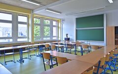 Blick in ein leeres Klassenzimmer mit Tafel, Tischen, Stühlen und Lehrerpult