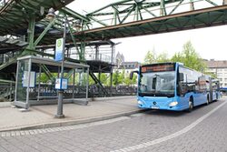 Blauer Gelenkbus an Haltestelle neben dem Schwebebahnhof - Schwebebahn-Express