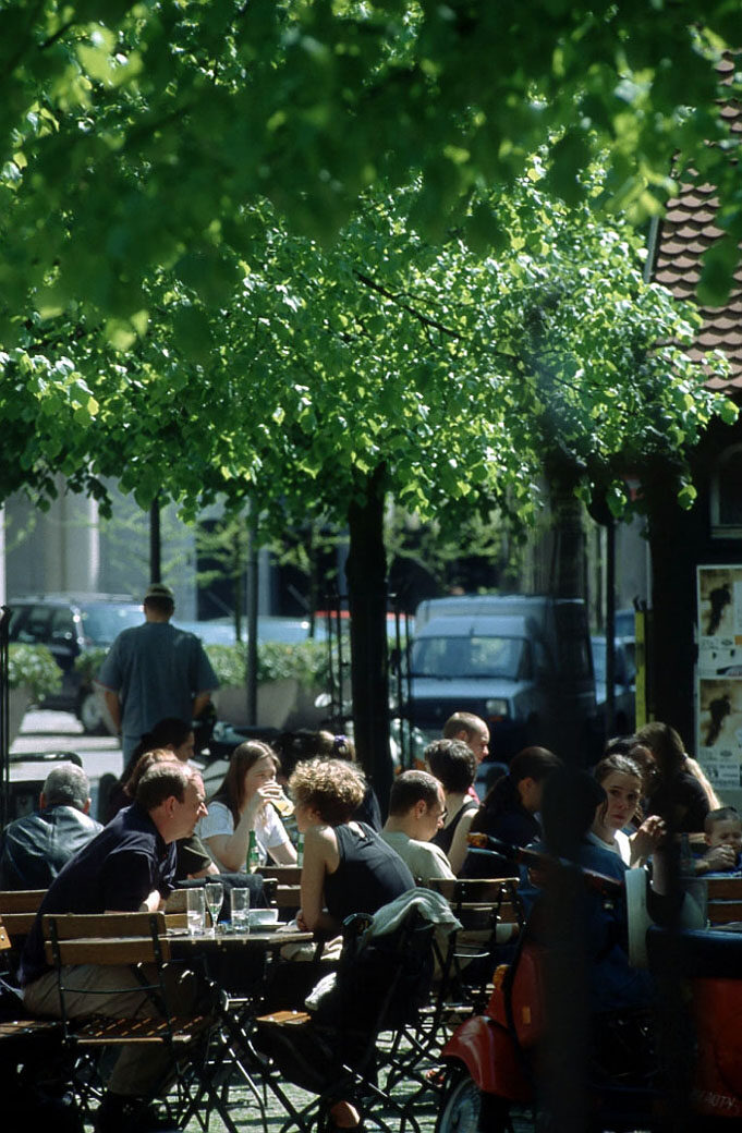 Außengastronomie mit Menschen an Tischen unter Bäumen