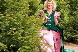 Märchenerzählerin Miss Fairytail sitzt im historischen Kostüm im Grünen und spielt mit einem goldenen Ball