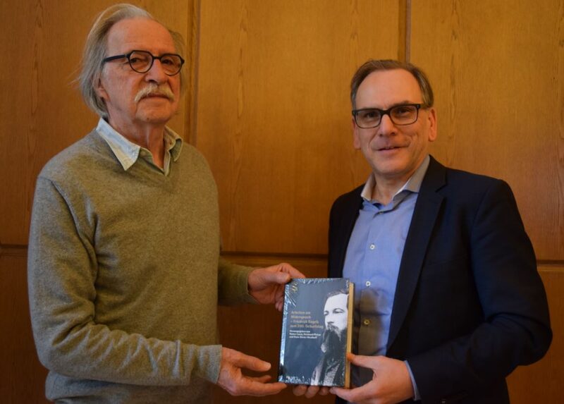 Kurator Hans-Dieter Westhoff überreicht Oberbürgermeister Mucke ein Werk über Engels, das er gemeinsam mit Kurator Rainer Lucas heraus gegeben hat