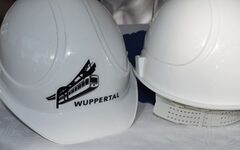 Zwei weiße Bauhelme, auf einem ist eine Schwebebahngrafik und das Wort "Wuppertal" zu sehen.