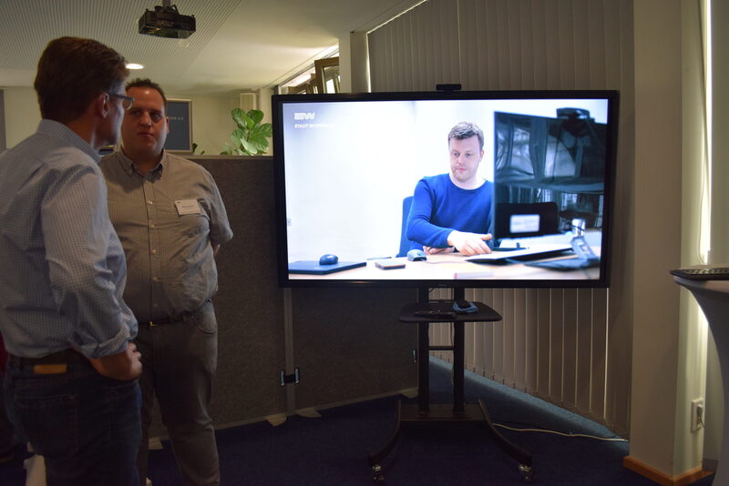 Video-Konferenz: Städtische Mitarbeiter sind über einen großen Monitor mit einem Kollegen an dessen Arbeitsplatz verbunden